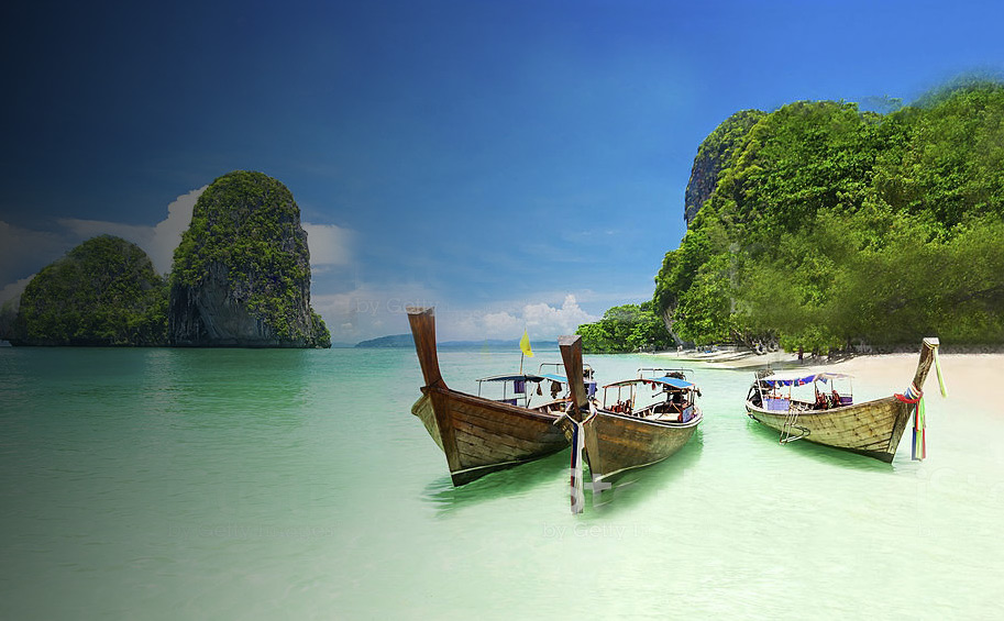 Thailändischer Strand mit klarem Wasser und Booten vor grünen Hügeln